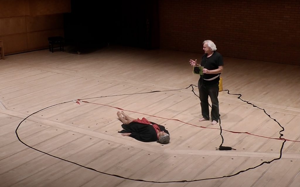 one person laying down and another standing within a circle drawn on the ground