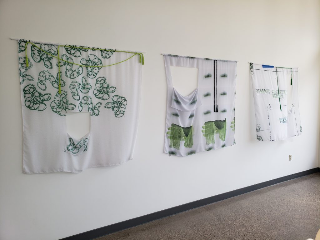 Three scarf-based artworks hanging on a white wall