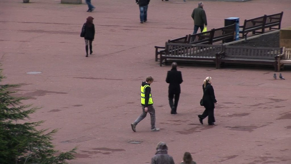 video still of person in reflective vest following other people